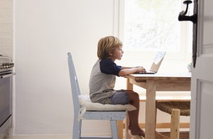 Young boy using laptop in kitchen, side view, from doorway